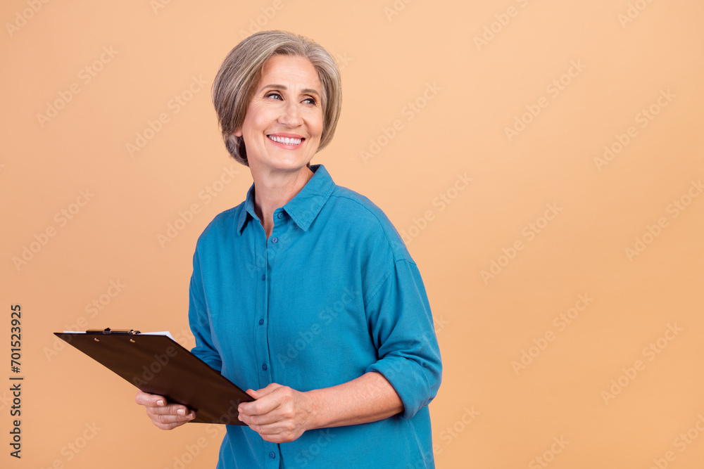 Poster Photo of retired woman with bob hairdo dressed blue shirt hold clipboard look at offer empty space isolated on pastel color background