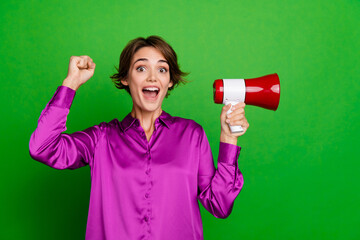 Photo of young crazy activist young funny woman holding megaphone raised fist up loud voice tool isolated on green color background