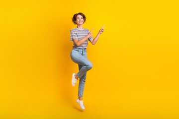 Fototapeta na wymiar Full size photo of nice cheerful girl jumping indicate fingers empty space proposition isolated on yellow color background