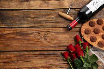 Red wine, chocolate truffles, corkscrew and roses on wooden table, flat lay. Space for text