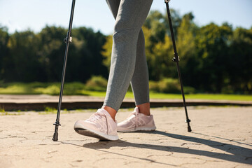Woman practicing Nordic walking with poles in park on sunny day, closeup