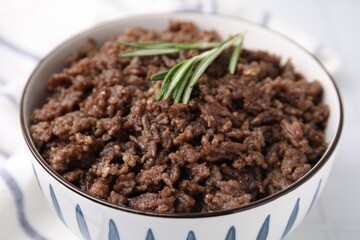 Fried ground meat in bowl and rosemary on table, closeup