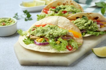Delicious tacos with guacamole, meat and vegetables on light grey table, closeup