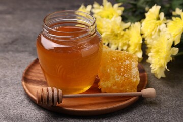 Sweet golden honey in jar, dipper and honeycomb on grey textured table, closeup