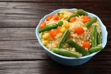 Delicious bulgur with vegetables in bowl on wooden table, closeup. Space for text