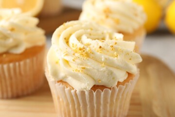 Tasty cupcakes with cream and lemon zest on wooden board, closeup