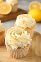 Tasty cupcakes with cream and lemon zest on wooden board, closeup