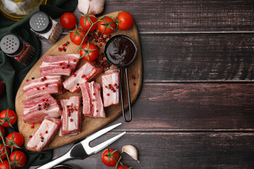 Flat lay composition with cut raw pork ribs and sauce on wooden table. Space for text