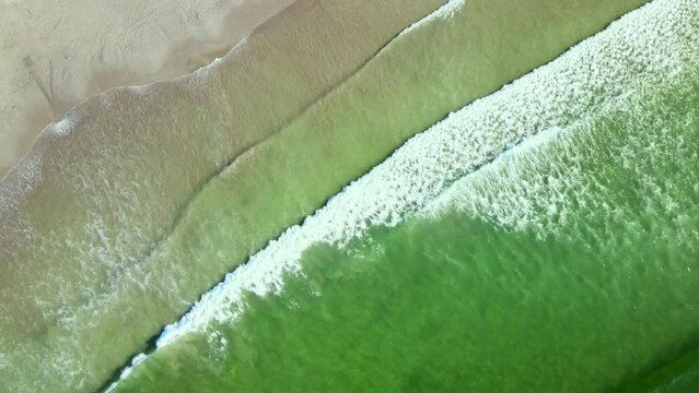 Diagonal top drone view as waves run out onto sandy beach from aquamarine ocean