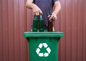 Closeup shot man holding glass beer bottles over recycle bin