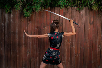 Side view Sexy samurai girl in Japanese dress holding katana sword, bamboo plant in background 