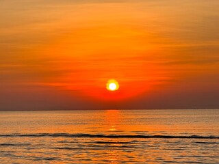 Sun going down in orange sky over horizon. Golden sunset at the sea with soft waves. Tropical sunset. Seascape and shore.
