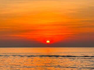 Sun going down in orange sky over horizon. Golden sunset at the sea with soft waves. Tropical sunset. Seascape and shore.
