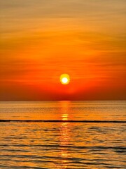 Sun going down in orange sky over horizon. Golden sunset at the sea with soft waves. Tropical sunset. Seascape and shore.
