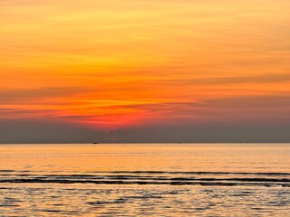 Sun going down in orange sky over horizon. Golden sunset at the sea with soft waves. Tropical sunset. Seascape and shore.
