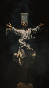 Jesus rises from smokey ashes on a dark black background with arms raised to the sky.