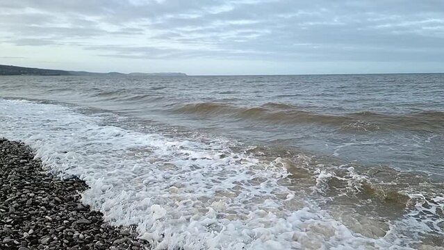 Sandy waves slow motion crash onto Llandudno pebble beach