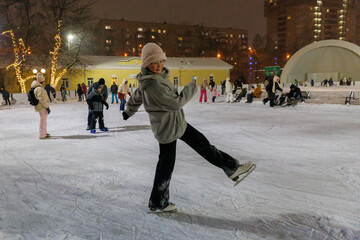 Funny moment fell on the ice skating rink. Holiday and seasonal concept. Teenager ice skating on public ice rink in park in evening