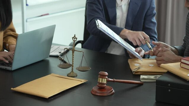 Asian legal team in meeting. woman and two men discussing over documents with law books and gavel on the table, indicating legal setting.