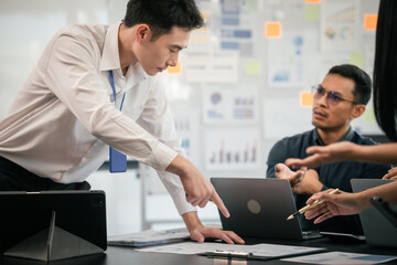 Fototapeta premium diverse group of Asian professionals, including middle-aged and mature individuals, gathered around a table in a business setting, discussing documents with focused attention.