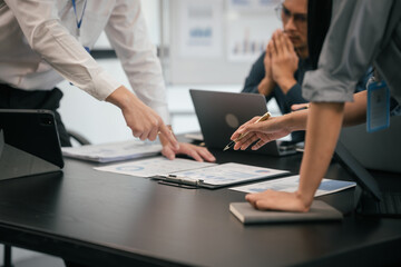 diverse group of Asian professionals, including middle-aged and mature individuals, gathered around a table in a business setting, discussing documents with focused attention. - obrazy, fototapety, plakaty