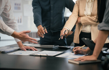 diverse group of Asian professionals, including middle-aged and mature individuals, gathered around a table in a business setting, discussing documents with focused attention.