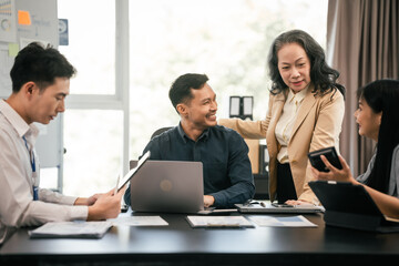diverse group of Asian professionals, including middle-aged and mature individuals, gathered around a table in a business setting, discussing documents with focused attention.