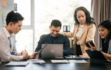 diverse group of Asian professionals, including middle-aged and mature individuals, gathered around a table in a business setting, discussing documents with focused attention.
