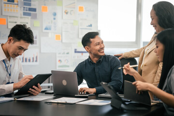 diverse group of Asian professionals, including middle-aged and mature individuals, gathered around a table in a business setting, discussing documents with focused attention.