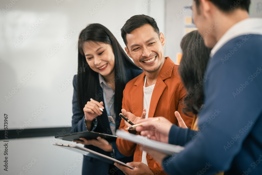 Wall mural Asian business professionals team actively engaged in collaborative meeting in boardroom, sharing opinions and working together with visible happiness.