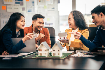 Asian real estate team engaged in a discussion, with two men and a woman focusing on a house model on a table, suggesting a planning or sales meeting.