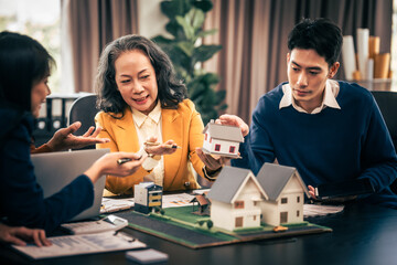 Asian real estate team engaged in a discussion, with two men and a woman focusing on a house model...
