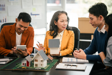 Asian real estate team engaged in a discussion, with two men and a woman focusing on a house model on a table, suggesting a planning or sales meeting.
