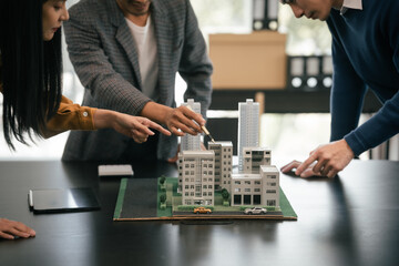 Asian team is engaged in a lively discussion over a scale model of a cityscape, likely representing a real estate or architectural project. - obrazy, fototapety, plakaty