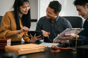 Asian legal team in meeting. woman and two men discussing over documents with law books and gavel on the table, indicating legal setting.