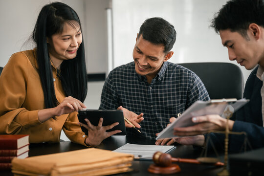Asian legal team in meeting. woman and two men discussing over documents with law books and gavel on the table, indicating legal setting.