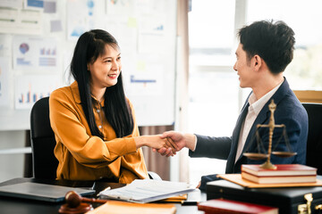 Asian man and woman collaborating professional setting, law office. reviewing documents on tablet, with laptop, contract papers, law books, and justice scale on the desk.