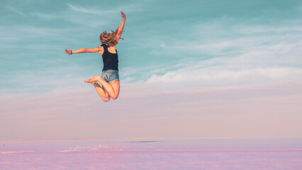 Carefree woman jumping on pink salt lake - active, wellness, healthy lifestyle concept