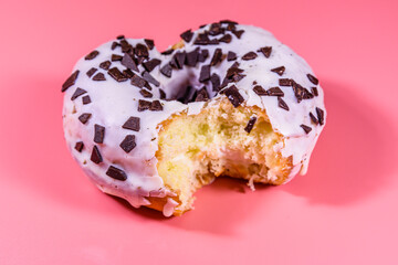Bitten glazed donut with chocolate chip on top isolated on a pink background