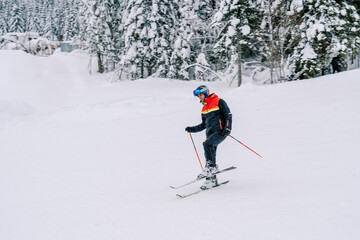 Man in a ski suit is skiing with his leg bent at the knee on the slope of a snowy mountain