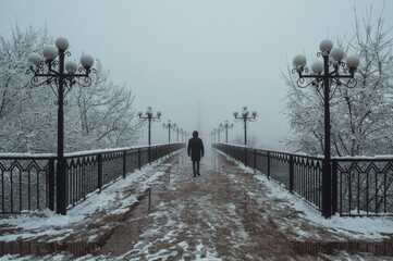 silhouette back man maniac walks on a foggy bridge with lanterns in winter with snow and fog