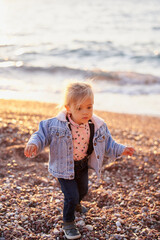 Little girl in a jacket walks along a pebble beach