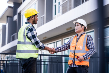 two construction workers, one Asian, shaking hands on a building site, possibly indicating...