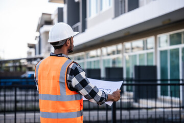 Obraz premium engineer in a high-visibility vest and hard hat, intently reviewing a document or blueprint, with a modern building in the background.
