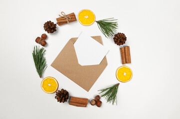 Christmas composition, circle, dried orange slices, fir tree branches, cinnamon sticks, pine cones, hazelnuts on white background. Kraft envelope, white card. Top view, flat lay, copy space.