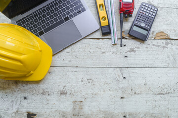 work environment with a laptop, a yellow hard hat, calculator, level, screwdriver, and folding...
