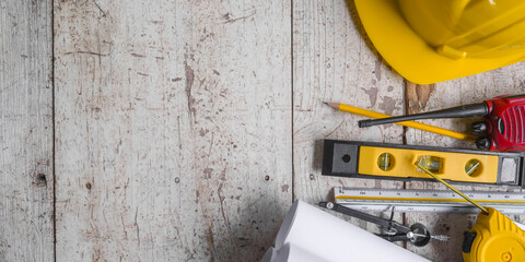 Top view construction tools such as a yellow hard hat, spirit level, measuring tape, folding ruler arrayed against a wooden plank background. - obrazy, fototapety, plakaty