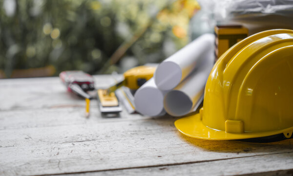 yellow safety helmet and rolled up architectural blueprints on a wooden desk, indicative of an architect's work area, possibly at a construction site.