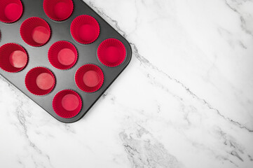 Top view of cupcake pan and silicone cases on white marble background. Muffins and cupcakes cooking, flat lay, copy space.