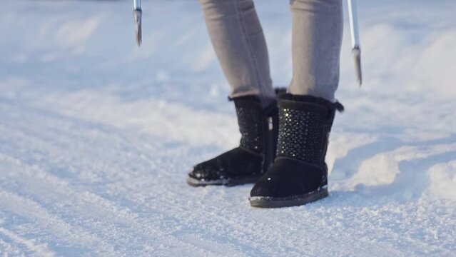 female legs in ugg boots with Scandinavian walking poles on snow-white clean snow. The sticks stick into the snow and the ice scatters. winter sports. activity in winter.